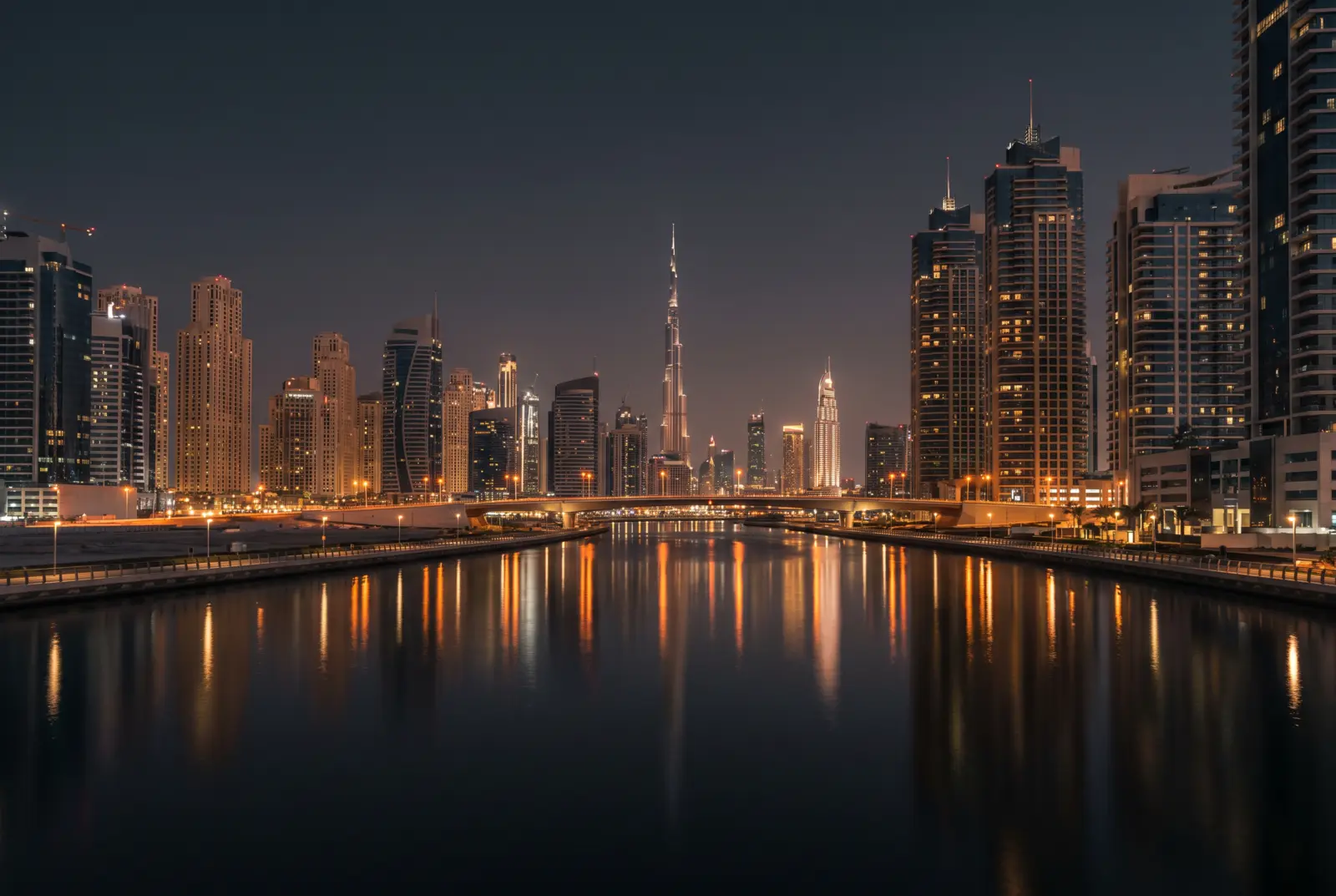 Business Bay canal at night reflecting illuminated towers, Burj Khalifa in the distance