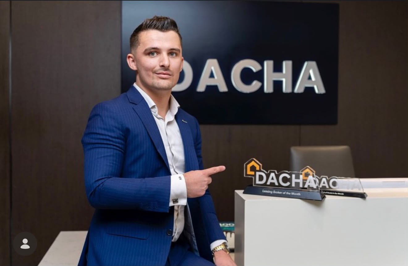 Matt Bougourd seated at the Dacha Real Estate office in Dubai, pointing to his Leasing Broker of the Month awards